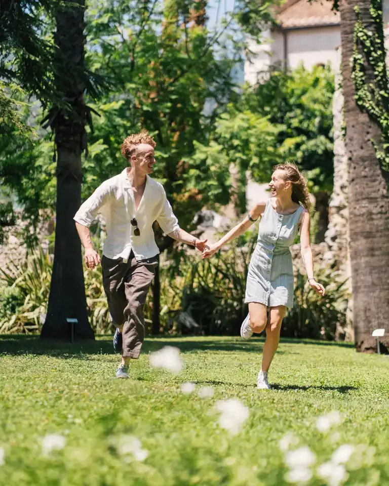 Couple running happily on a field of green grass in the garden of Villa Rufolo looking happy