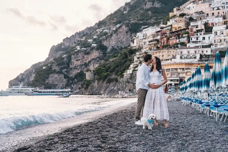 Couple holding each other with their petite dog walking by Spiaggia Grande in Positano