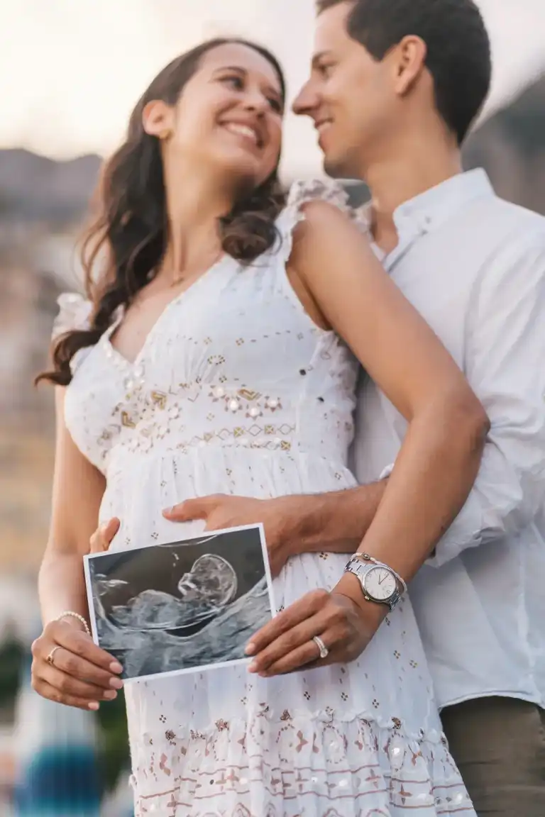 A man hugging her attending fiancé while she holds the ultrasound picture of their baby
