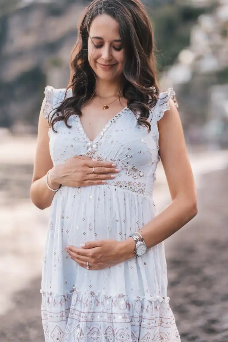 Mother holding her belly and looking down to it wearing a soft, eery dress
