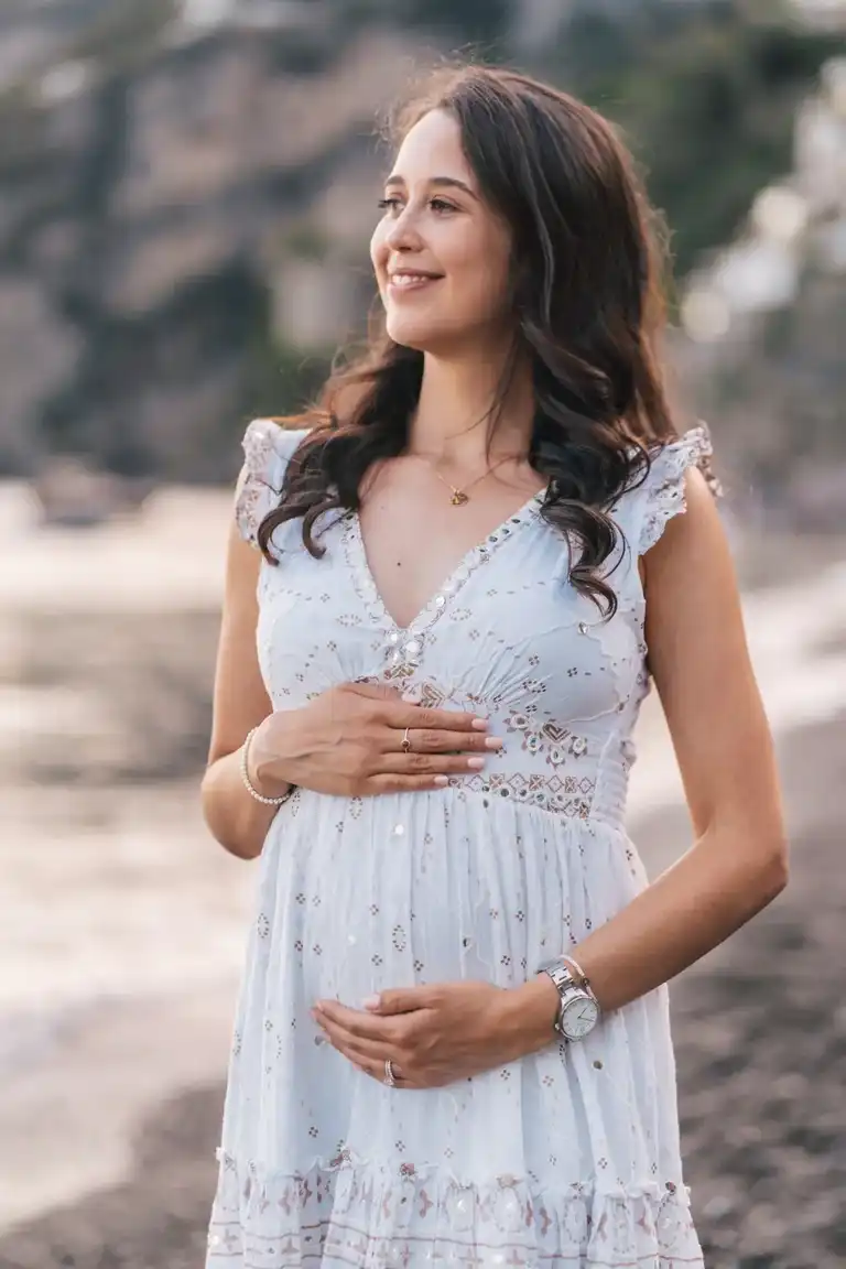 Woman looking at the sea in front of Positano holding her belly in a maternity pose while she smiles