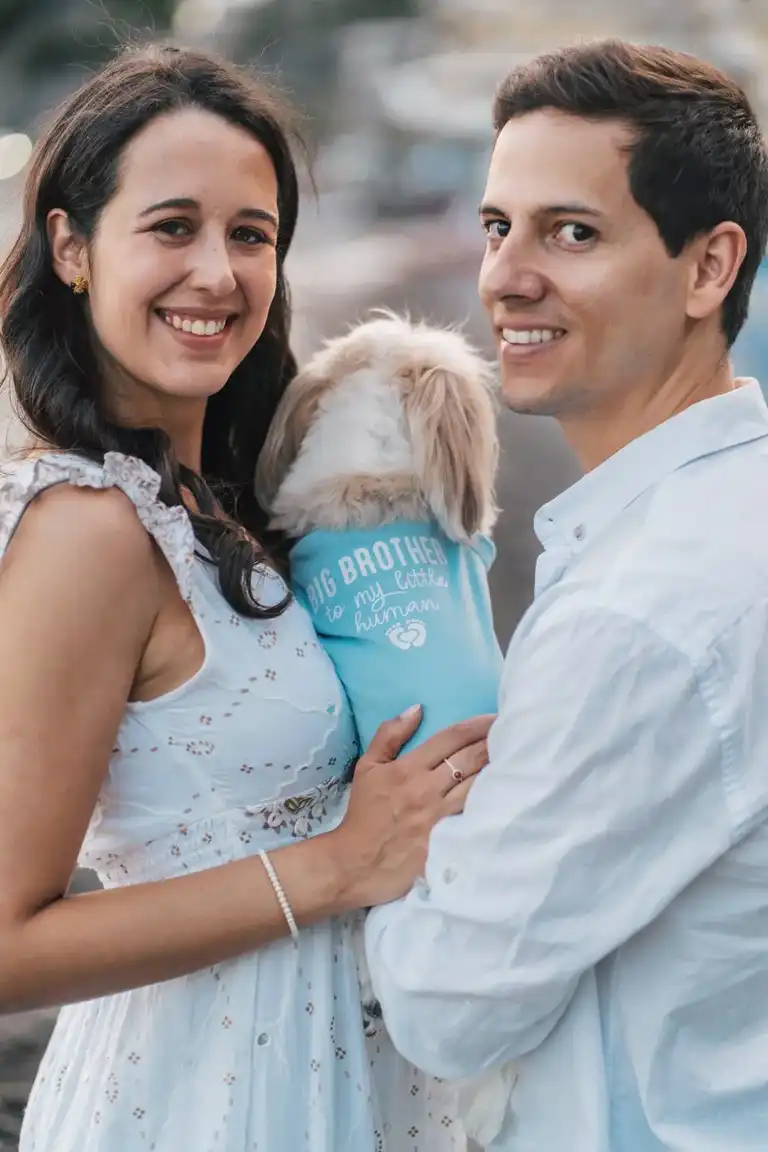 A mand and a woman holding their dog wearing a cute shirt smiling to the camera