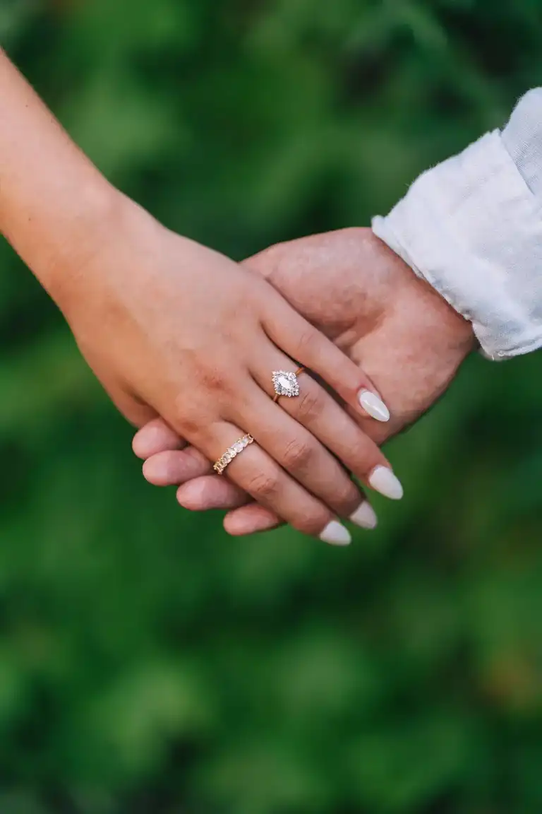 couple holding hands showcasing engagement ring with green out of focus background