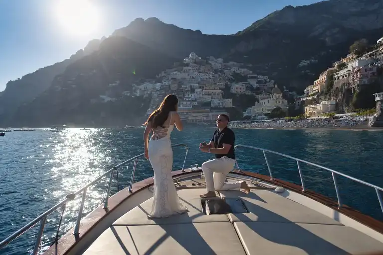 Surprise proposal on a boat with Positano in the backdrop, the man is on his knee asking the question to his girlfriend