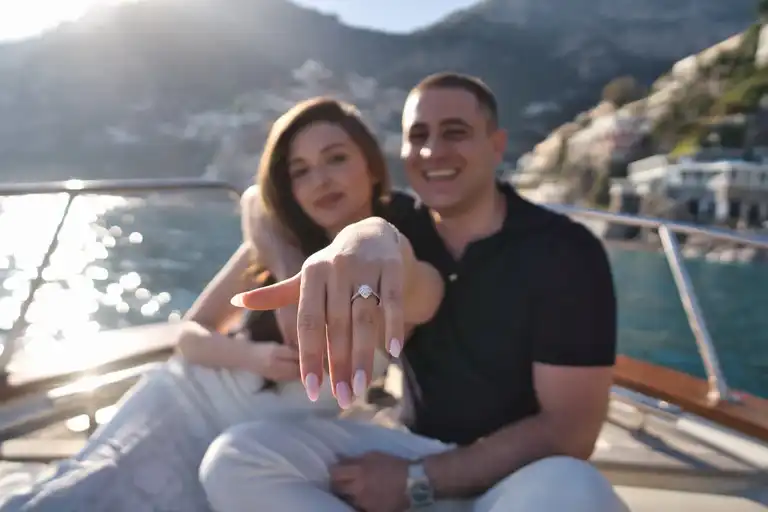 Happy couple on boat sitting down as they show to the camera the ring - he just proposed to her and she said yes!