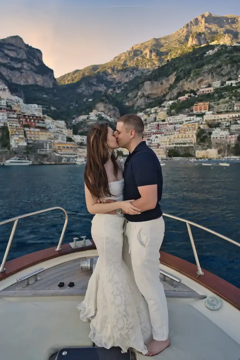 Couple standing on a boat in front of Positano kissing romantically during golden hour