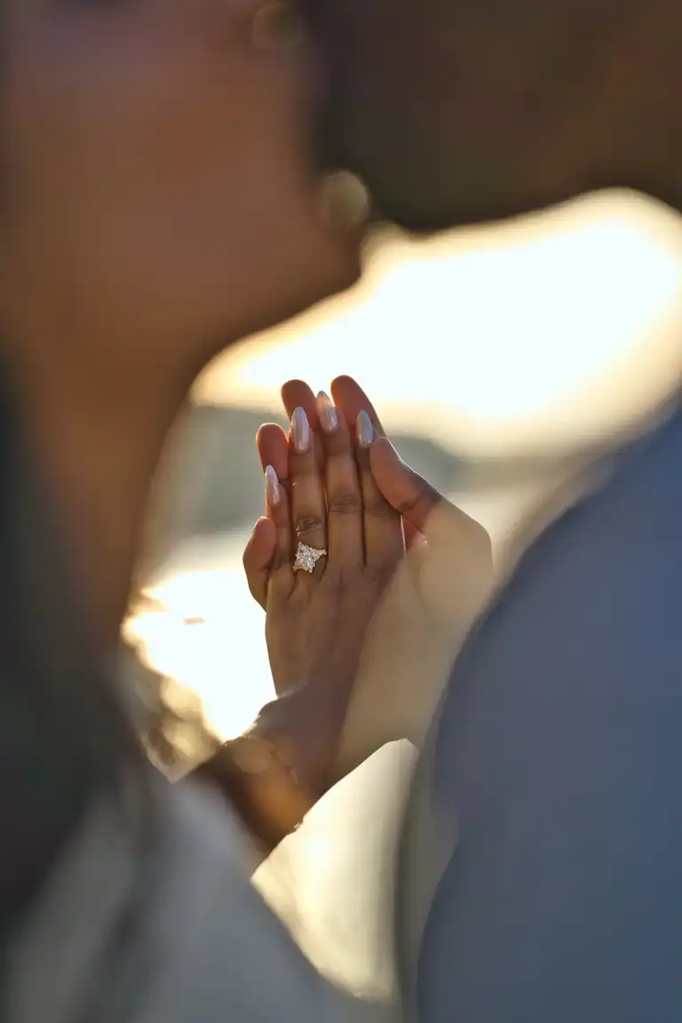 Blurry foreground of a couple kissing while their hands and the proposal ring is in focus in the background