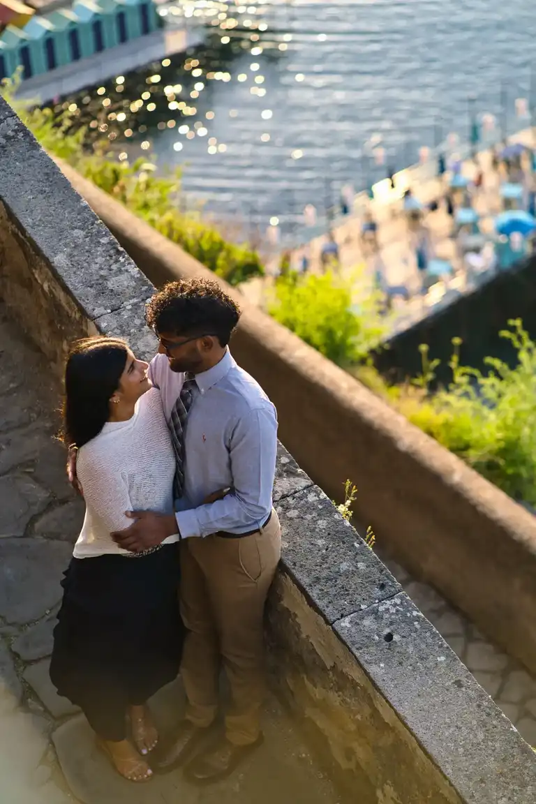 Couple holding each other on  the steps of Villa Comunale with the beach of Sorrento in the backdrop
