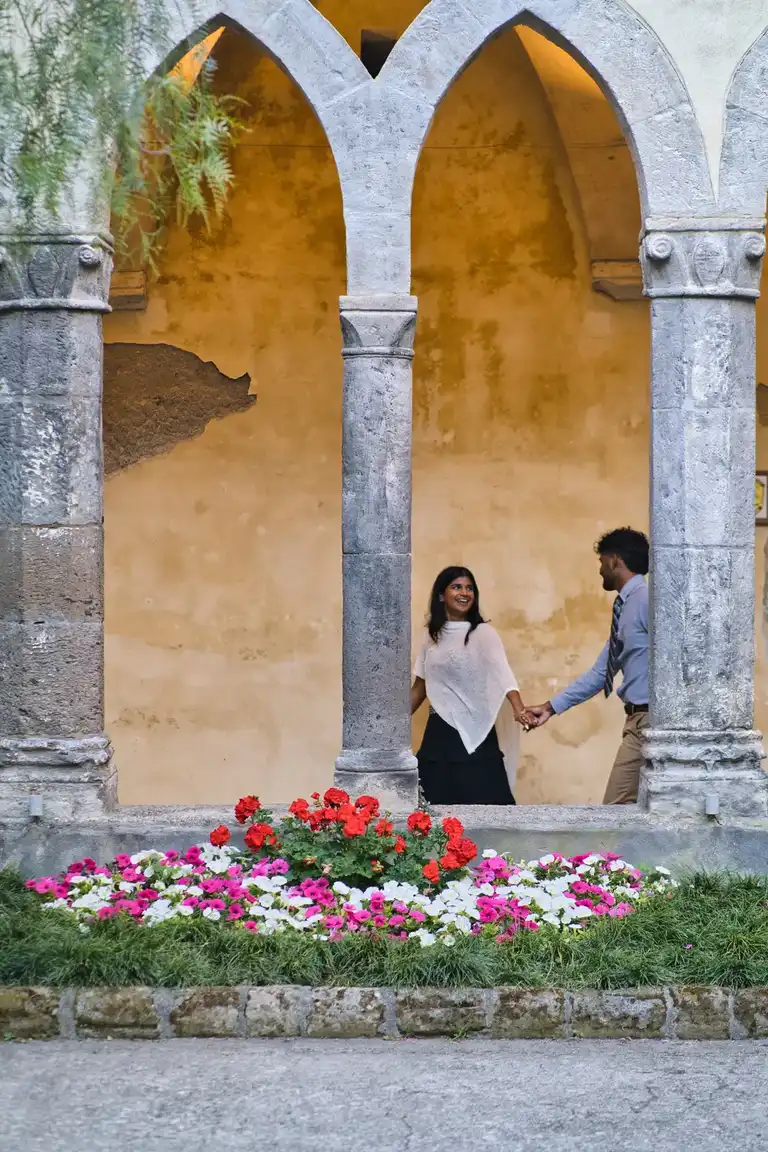 Couple holding hands in the cloister of San Francesco in Sorrento between arches and flowers