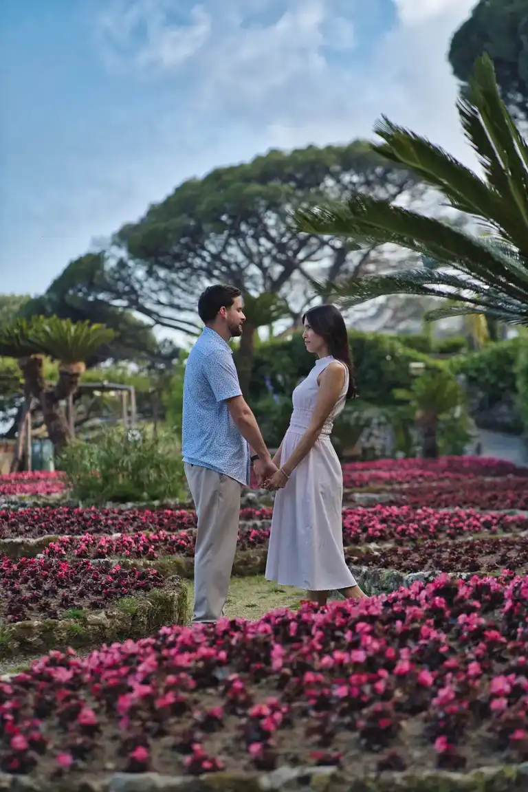 Couple holding hands facing each other immersed by the flowers of the garden terrace in Villa Rufolo, Ravello