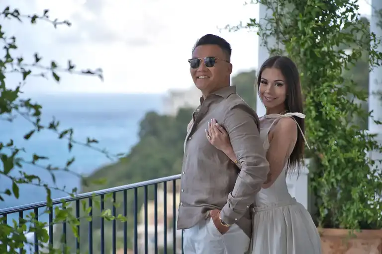 The bride and groom embrace gently on a scenic stone balcony at Borgo Sant'Andrea, overlooking the vast blue sea and the Amalfi coastline.