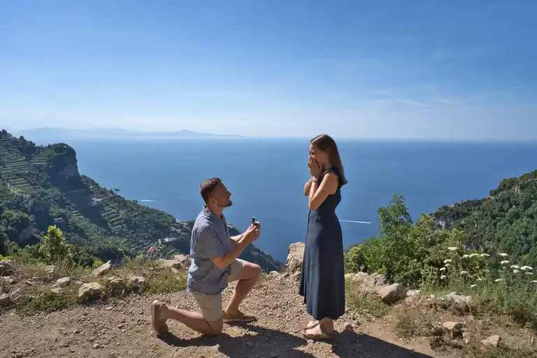 Secret proposal moment on a remote rocky outcrop along the Path of the Gods (Sentiero degli Dei) hiking trail from Bomerano, with the Mediterranean Sea and mountain ridges in the early morning light.