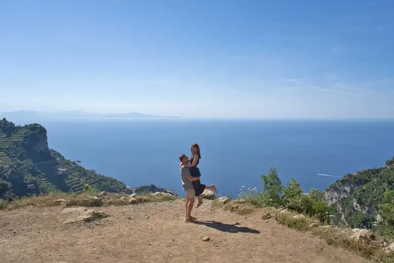 Couple on a mountain cliff overlooking the Mediterranean Sea and Amalfi Coast mountains during a early morning hike on Sentiero degli Dei.