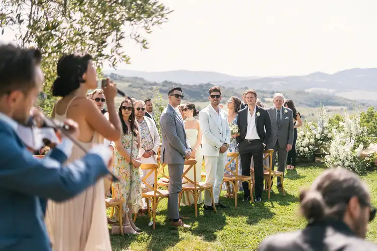 Broom and bride getting applauded before the ceremony starts with tuscany hills in the background