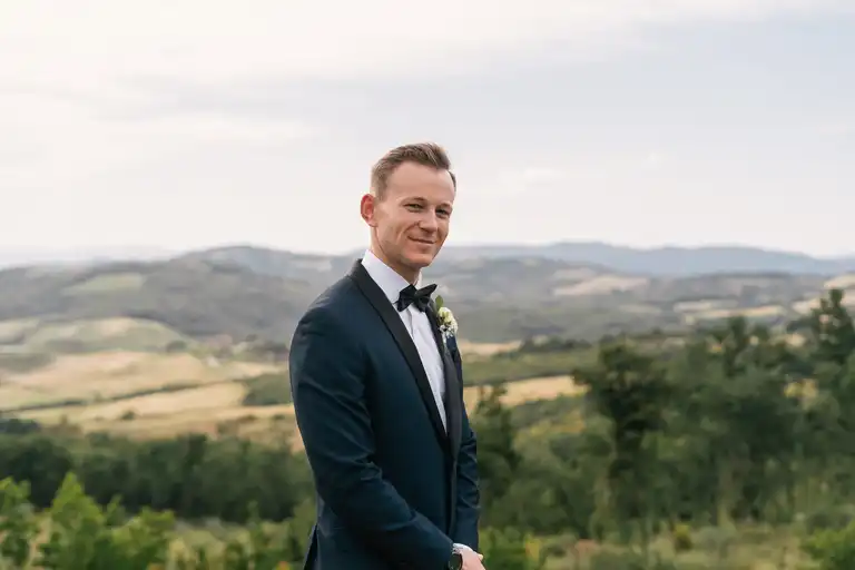 Broom posing handsomely in luxurious wedding dress with tuscany hills in the background