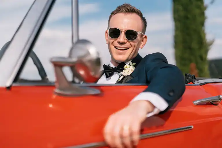 Broom playfully posing for the camera while driving a vintage italian car colored red