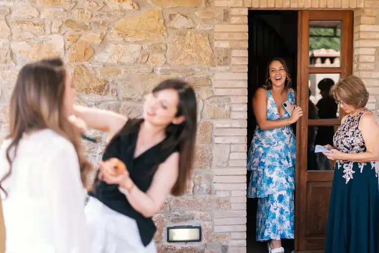 Bride getting ready with her make up artist while her sister and mom peek at the work being done on her